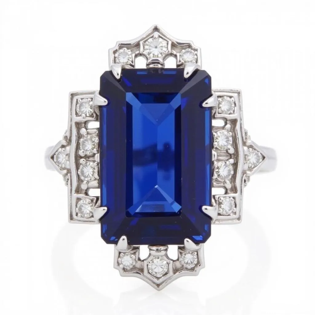 Art Deco cocktail ring featuring a large emerald-cut sapphire in a platinum setting, surrounded by smaller diamonds that form a geometric pattern around the stone.