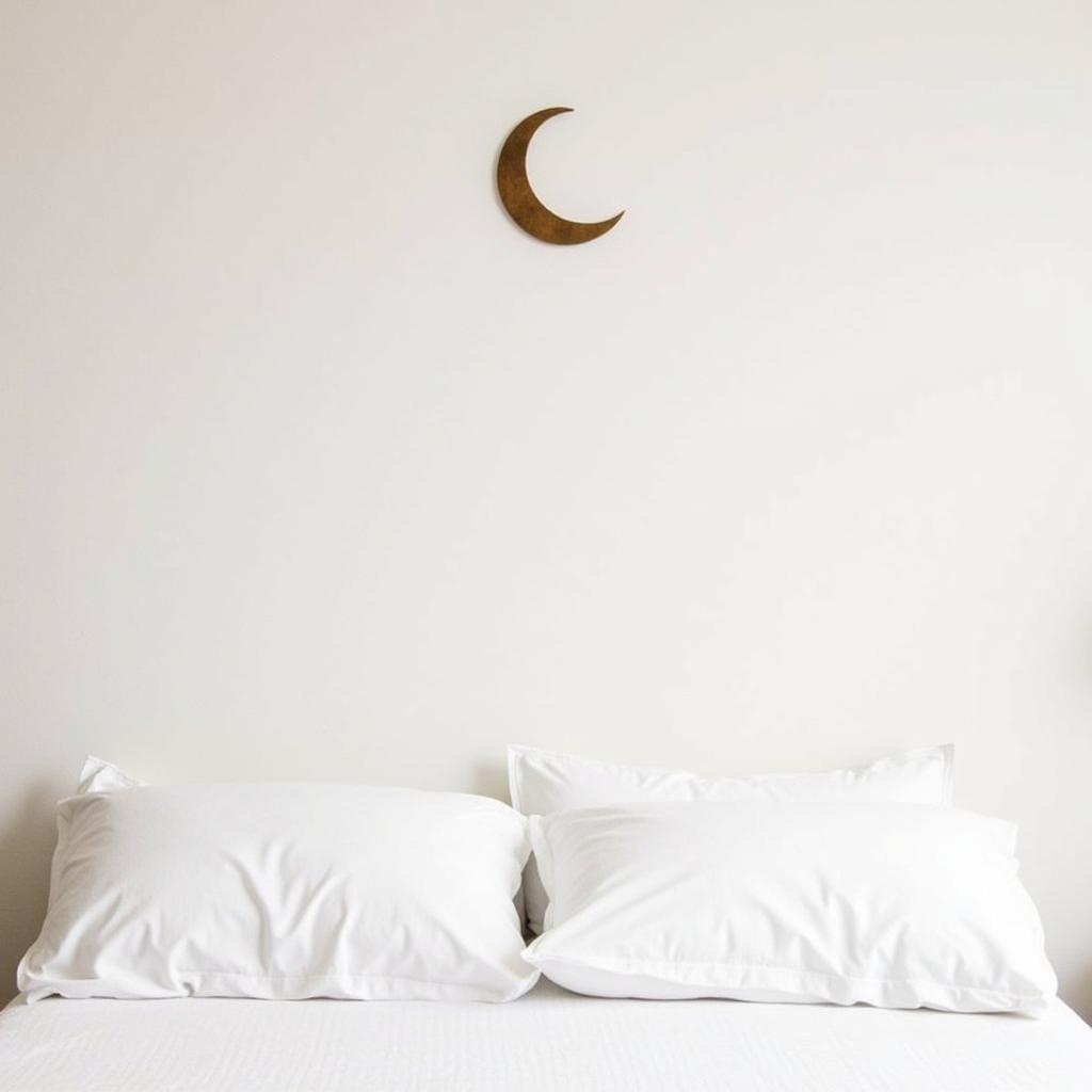 A delicate crescent moon metal wall art piece hangs above a bed in a minimalist bedroom.