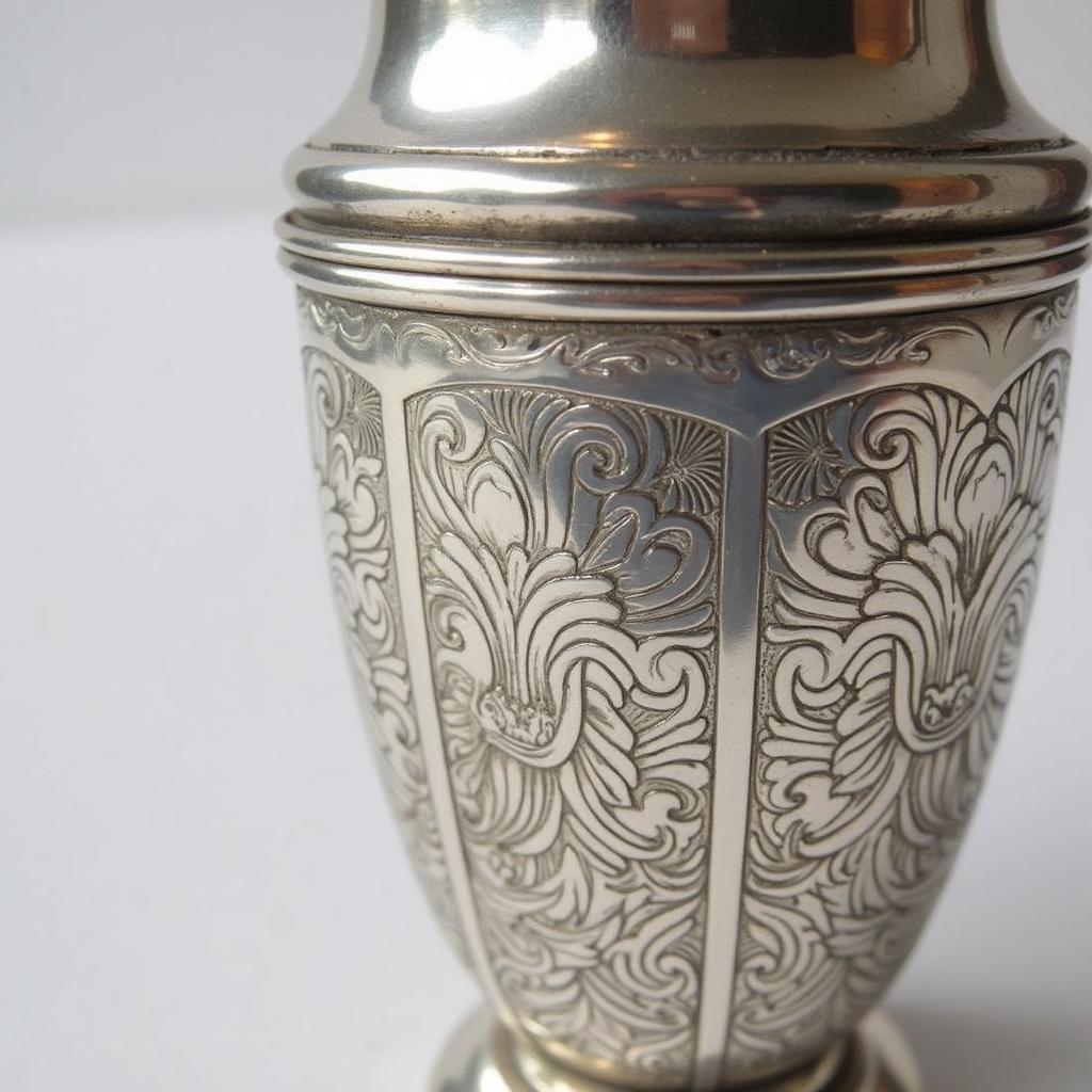 A close-up view of a vintage art deco cocktail shaker, showcasing its intricate geometric engravings and gleaming silver finish.